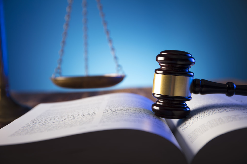 a gavel sitting atop an open law book with a scale in the background