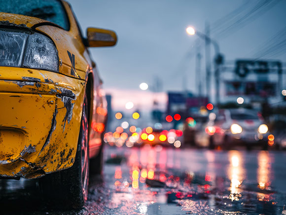 Raindrops and reflections on a wet New York City street with a yellow taxi in the foreground, illustrating traffic conditions linked to NYC taxi accidents