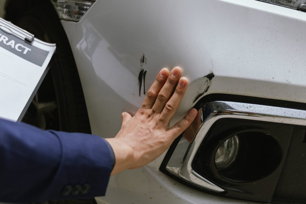 Hand examining vehicle damage on a white car, illustrating the purposeful evidence gathering performed by a New York City car accident lawyer.