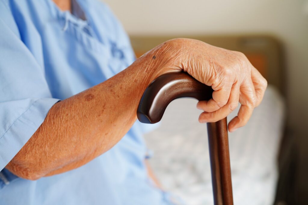 Close-up of an elderly person's hand gripping a wooden cane, illustrating the physical vulnerability of residents protected by a New York City nursing home abuse lawyer.