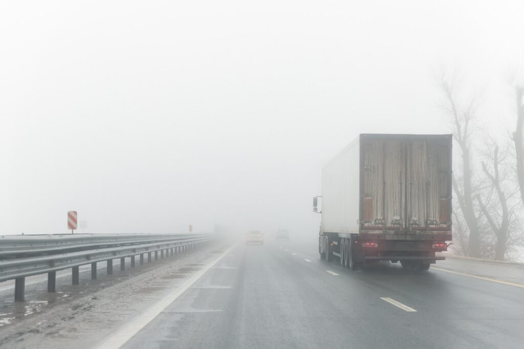 A large commercial freight truck driving through heavy fog on a Nueva York highway, illustrating hazardous conditions that require investigation by a New York City truck accident lawyer.