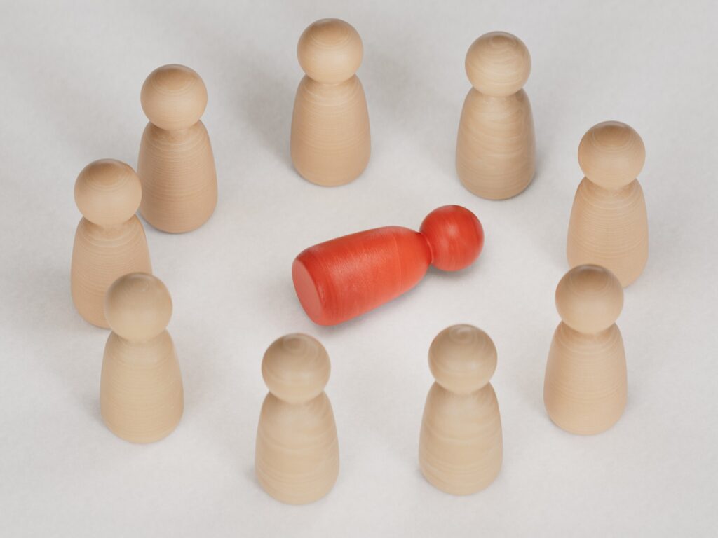 A red wooden figure isolated from a group, representing workplace exclusion and bias addressed by a New York City workplace discrimination lawyer.