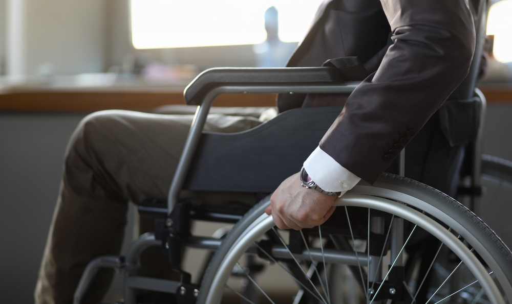 Close-up of disabled man on wheelchair in office wearing presentable suit. Adaptation of people with disabilities in society. Recovery and healthcare concept